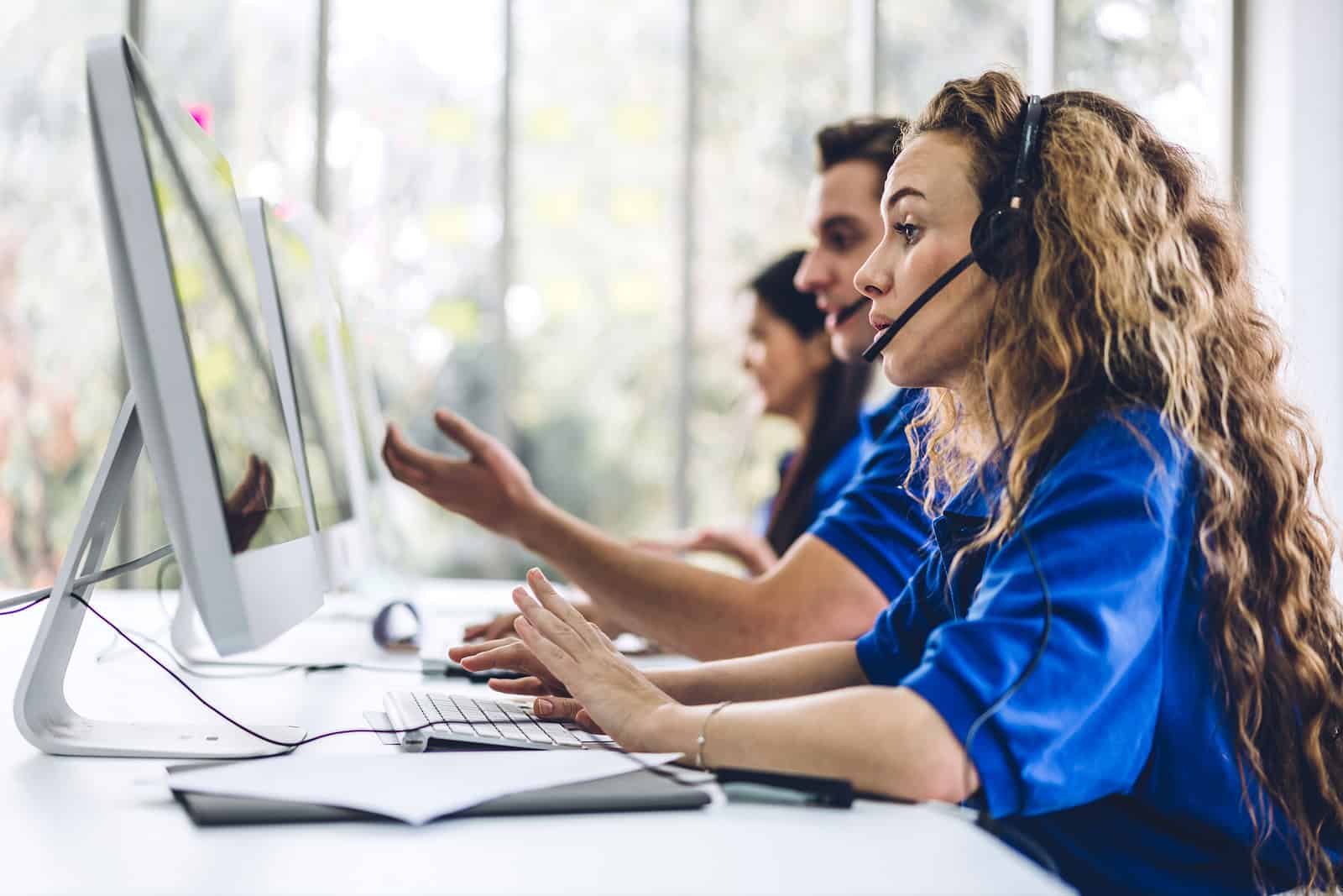 Call center customer service agents working with headsets on computers.