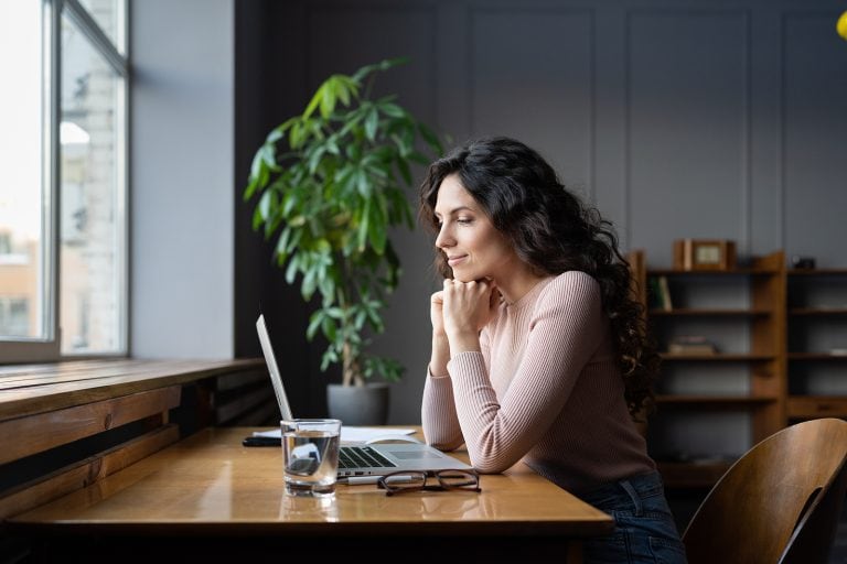 Woman working on laptop with email sign-offs on screen in cozy office setting.