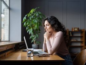 Woman working on laptop with email sign-offs on screen in cozy office setting.